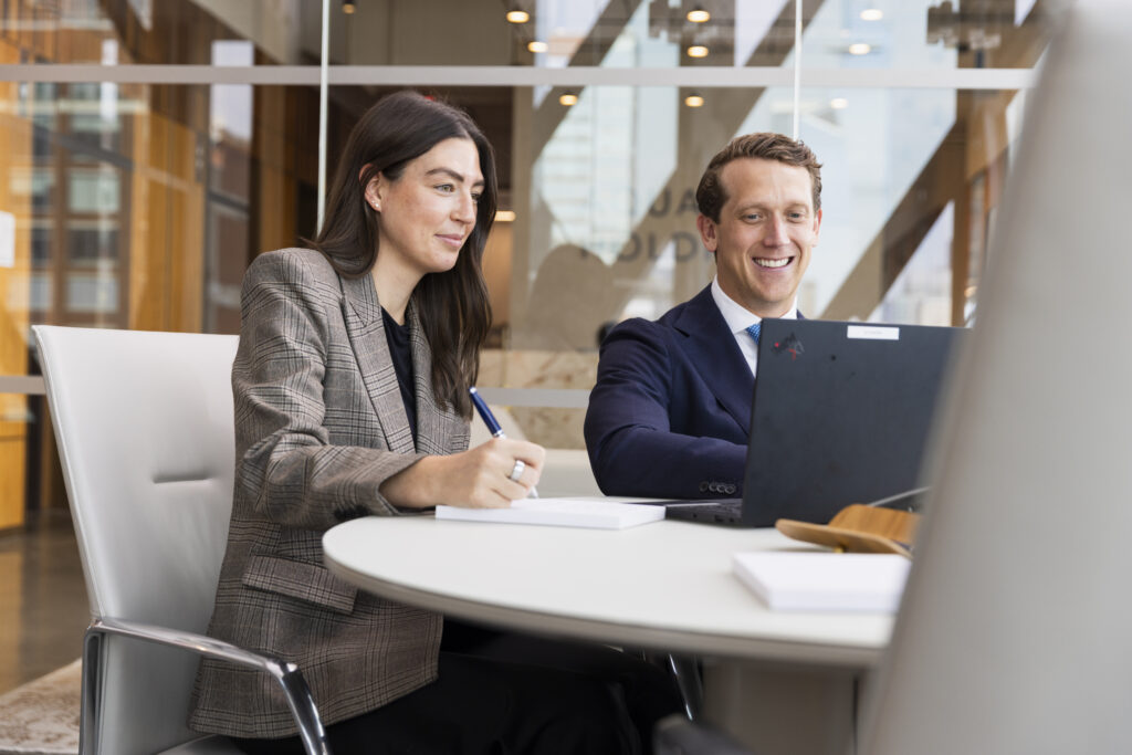 two people sitting together at a table looking at a laptop screen